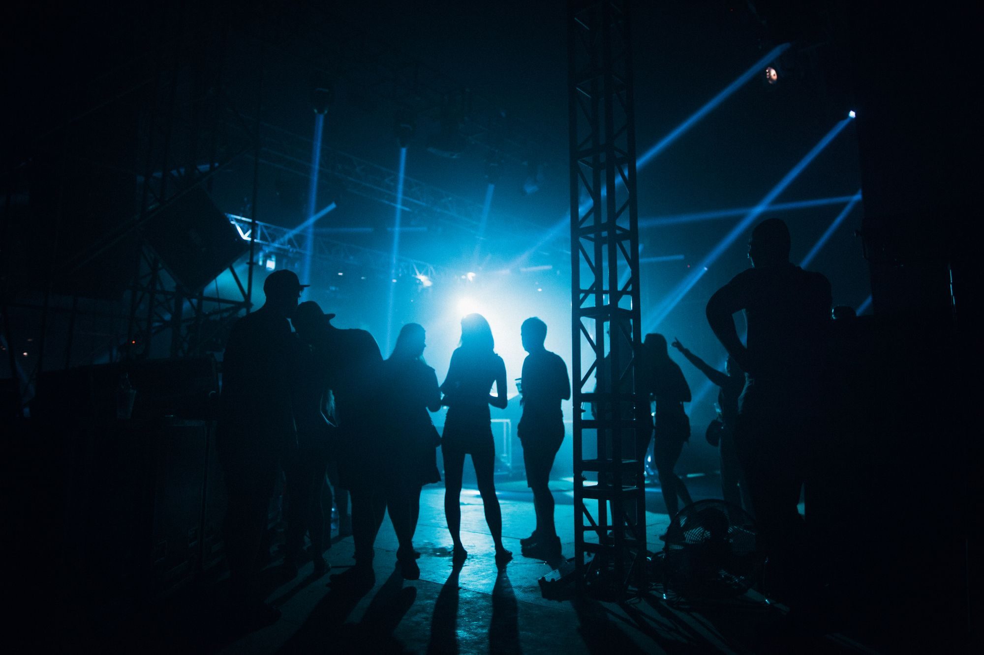 Silhouettes of crew and performers backstage under blue stage lights
