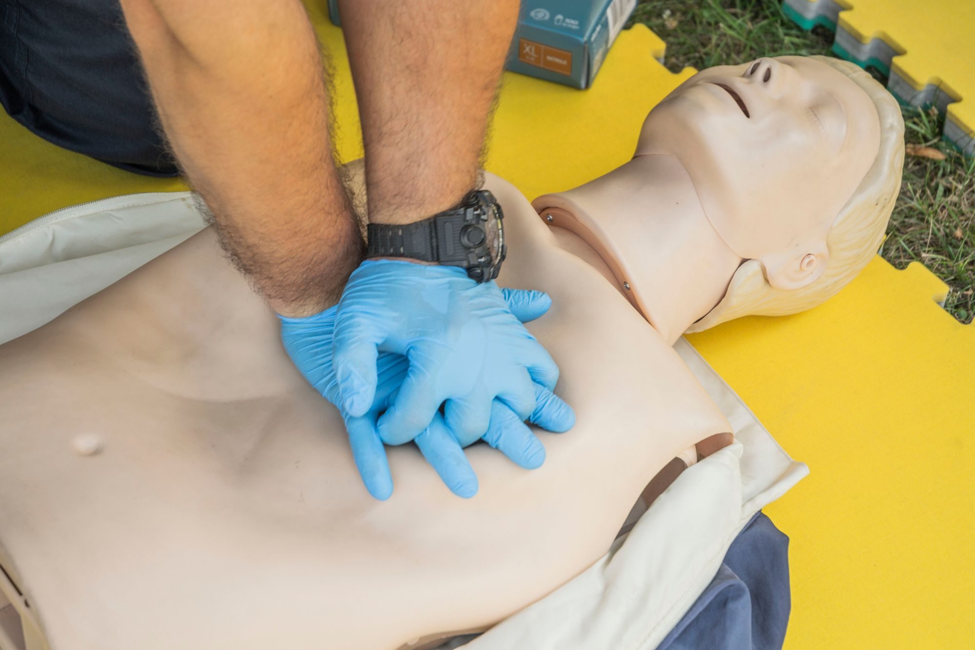 Gloved hands performing chest compressions on a training manikin