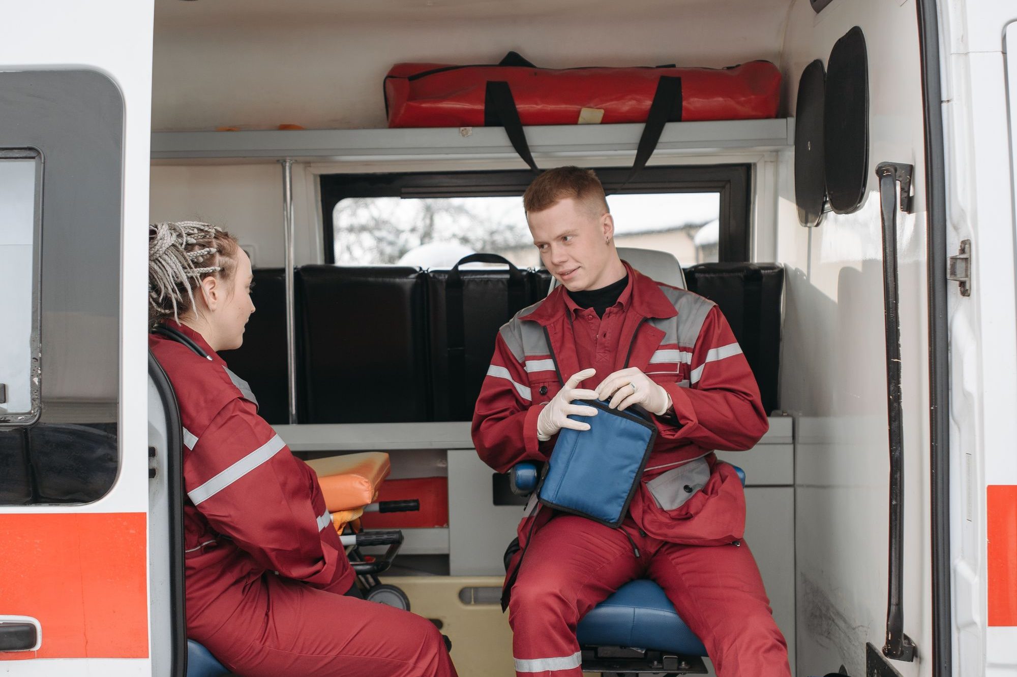 Two paramedics in red uniforms sitting in the back of an ambulance