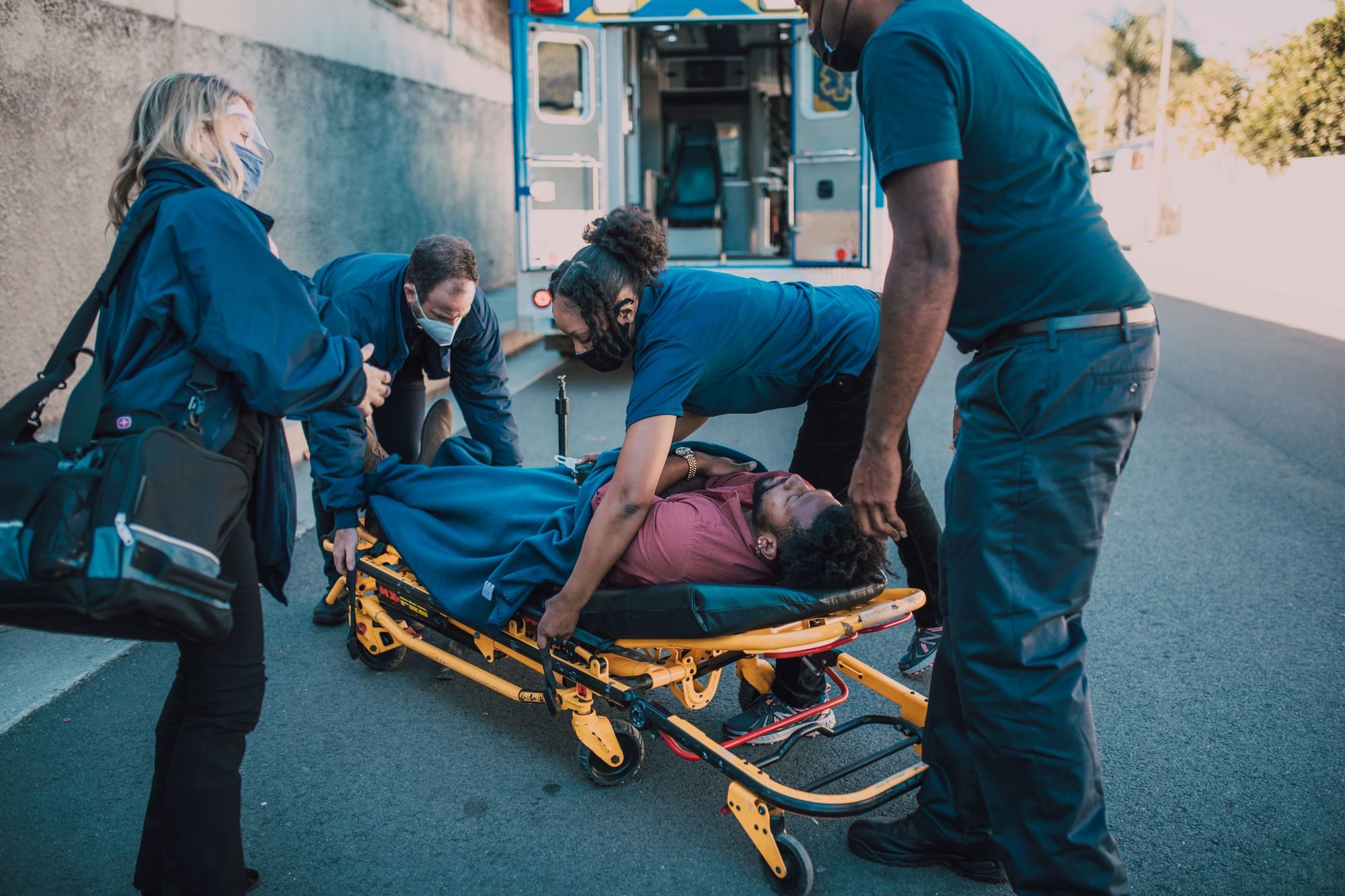 Paramedics helping a patient onto a stretcher beside an ambulance