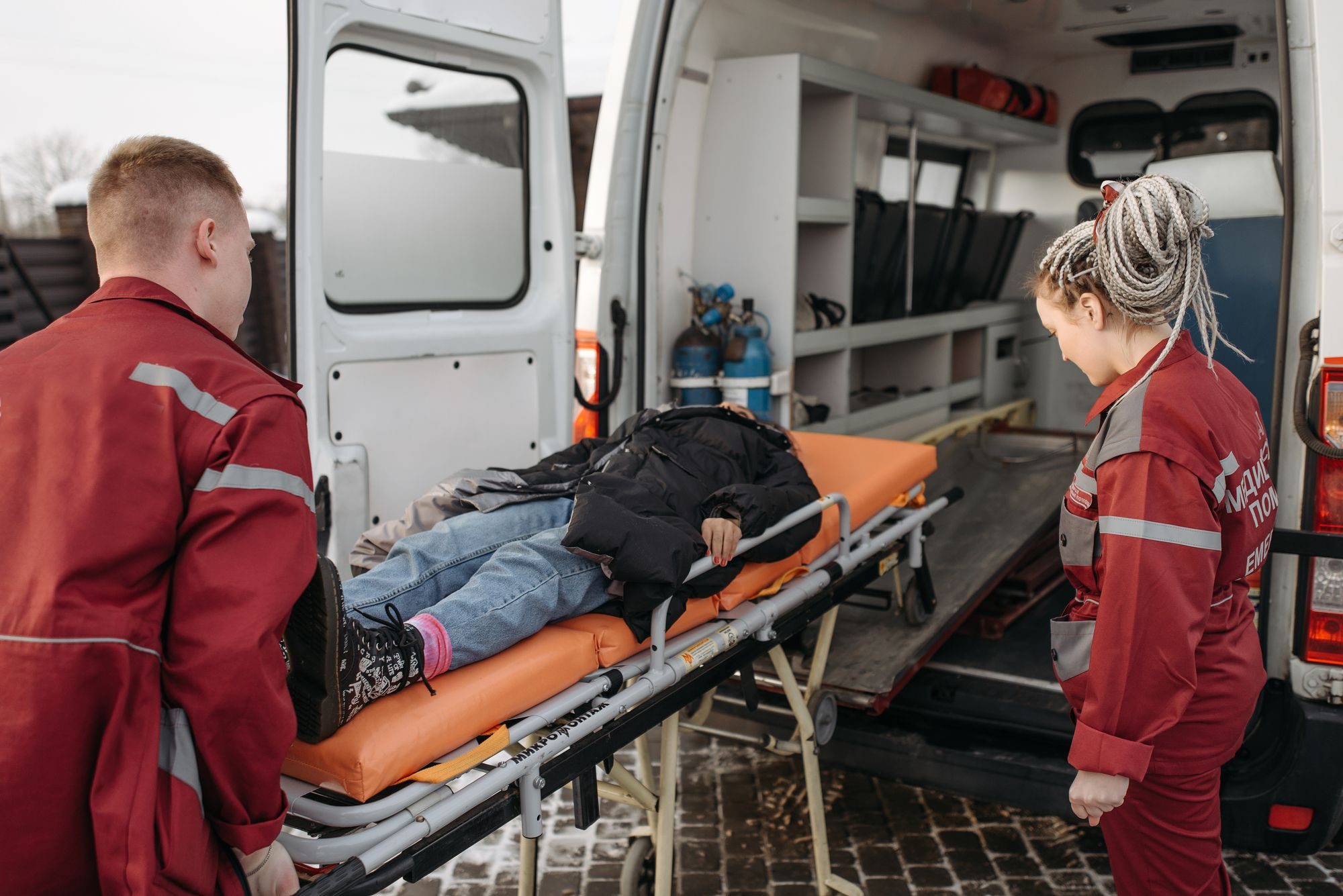 Paramedics in red uniforms loading a patient on a stretcher into an ambulance