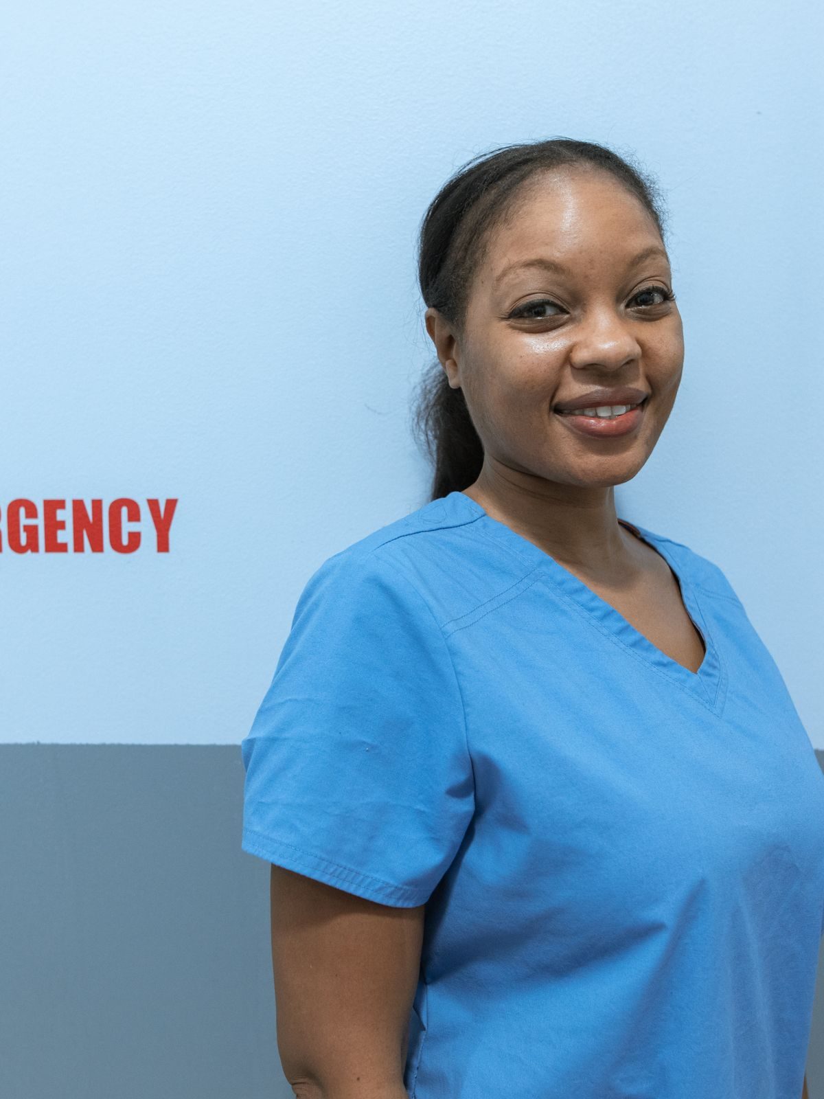 A nurse in blue scrubs standing by an emergency department sign
